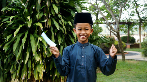 Smiling boy with envelope standing against plants