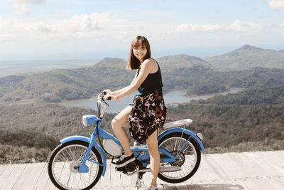 Portrait of smiling woman sitting on motorcycle against mountain range