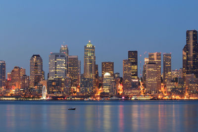 Illuminated buildings by river against sky in city