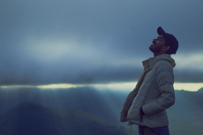 Side view of young man looking away against sky