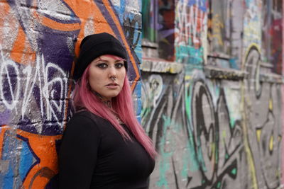 Portrait of young woman with pink hair standing against graffiti wall