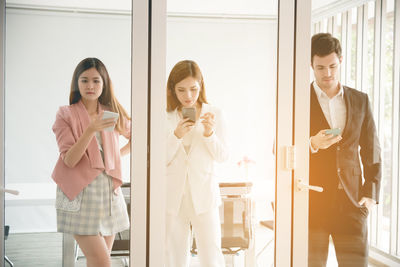 Colleagues reflecting on cabinet mirror while using phones in office