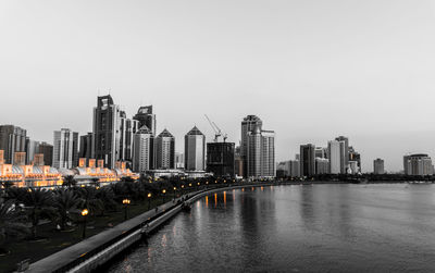 Illuminated city by river against clear sky