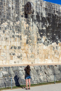 Rear view of woman photographing by weathered wall