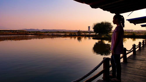 Reflection of woman on lake against sky during sunset
