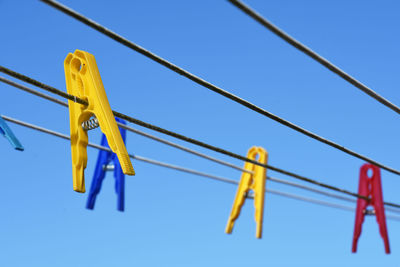 Low angle view of clothespins on clothesline against clear blue sky