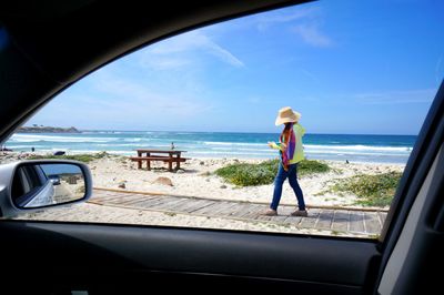 Woman walking on boardwalk at beach seen from car window