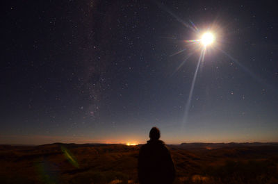 Rear view of man against moonlight in sky at night