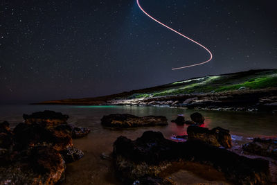 Scenic view of sea against light trail in sky at night