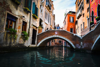 Man standing on arch bridge over channel amidst old buildings