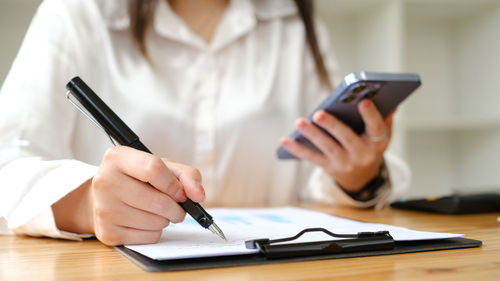 Midsection of woman using mobile phone at table