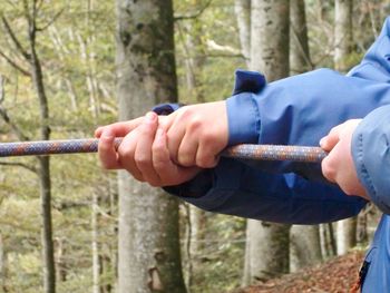 Close-up of hands pulling rope in forest