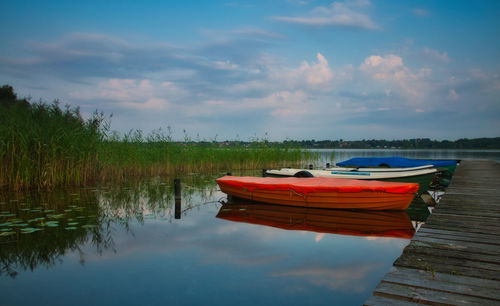 Boats moored by pier on lake against sky