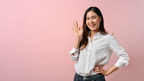Portrait of young woman standing against yellow background