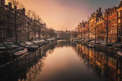 Canal amidst buildings in city against sky at sunset