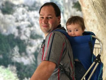 Side view portrait of man carrying baby boy in carrier against mountain