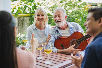 Smiling senior man playing guitar while sitting with friends at table