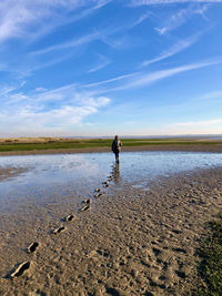 Rear view of a woman leaving footprints on mudflats near the sea, under blue sky