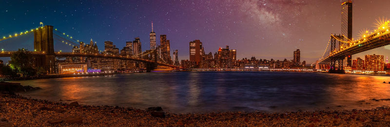 Illuminated bridge over river with buildings in background at night