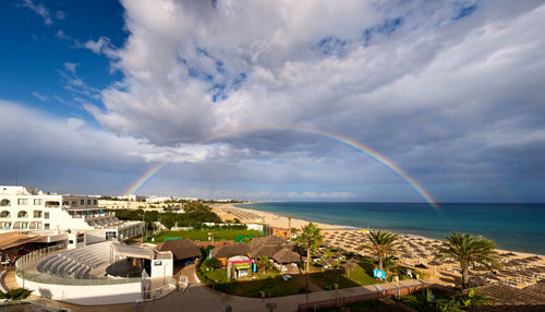 Scenic view of rainbow over sea and buildings against sky