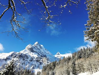 Low angle view of snowcapped mountains against blue sky