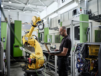 Male engineer using laptop by robotic arm