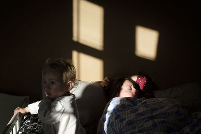 Baby girl looking away while mother sleeping on bed at home