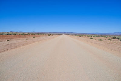 Road amidst desert against clear blue sky