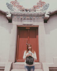 Portrait of smiling young woman standing against building