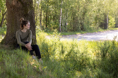 Young brunette woman sitting in green forest enjoys the silence and beauty of nature