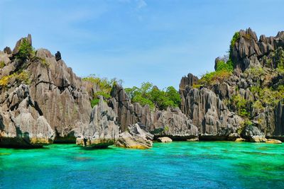 Rock formations by sea against blue sky