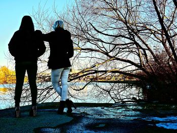 Rear view of silhouette couple standing against bare trees during winter