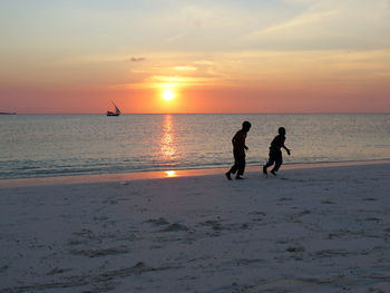 Silhouette boys playing at beach against sky during sunset