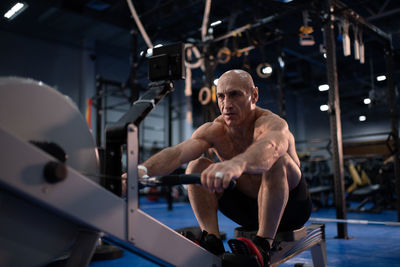 Tough senior sportsman doing rowing exercise in gym