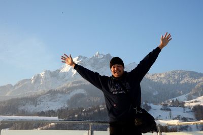 Smiling man with arms outstretched standing against mountain