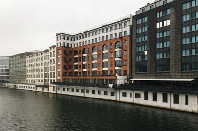 Buildings by river against sky in city