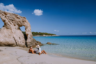 Woman sitting on beach by sea against sky