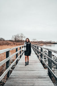 Portrait of woman walking on footbridge against sky