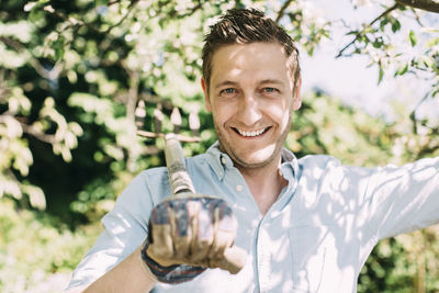 Portrait of happy man carrying gardening fork on shoulder at yard