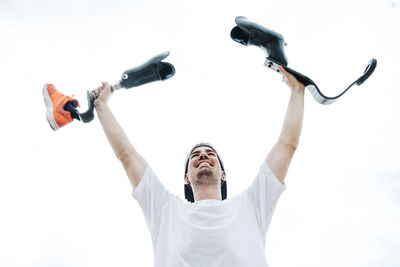 Happy young man with leg prosthesis cheering under cloudy sky