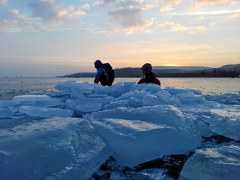 Siblings by ice formation against sky during sunset