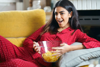 Portrait of smiling young woman in watching television sitting on sofa