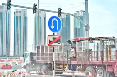 View of a construction truck passing a no trucks allowed sign with high rise buildings in background 