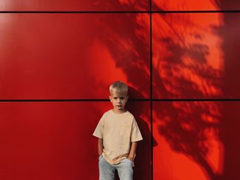 Portrait of boy standing against red wall