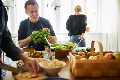 Mature men preparing food while female friend standing in background at home