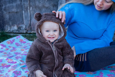 Portrait of smiling cute baby boy with his mother sitting on a mat on the grass.