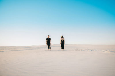 People walking on desert against clear sky