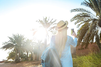 Rear view of woman standing by palm trees against sky