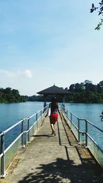 Rear view of man on railing by lake against sky