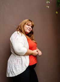 Portrait of a smiling young woman standing against wall